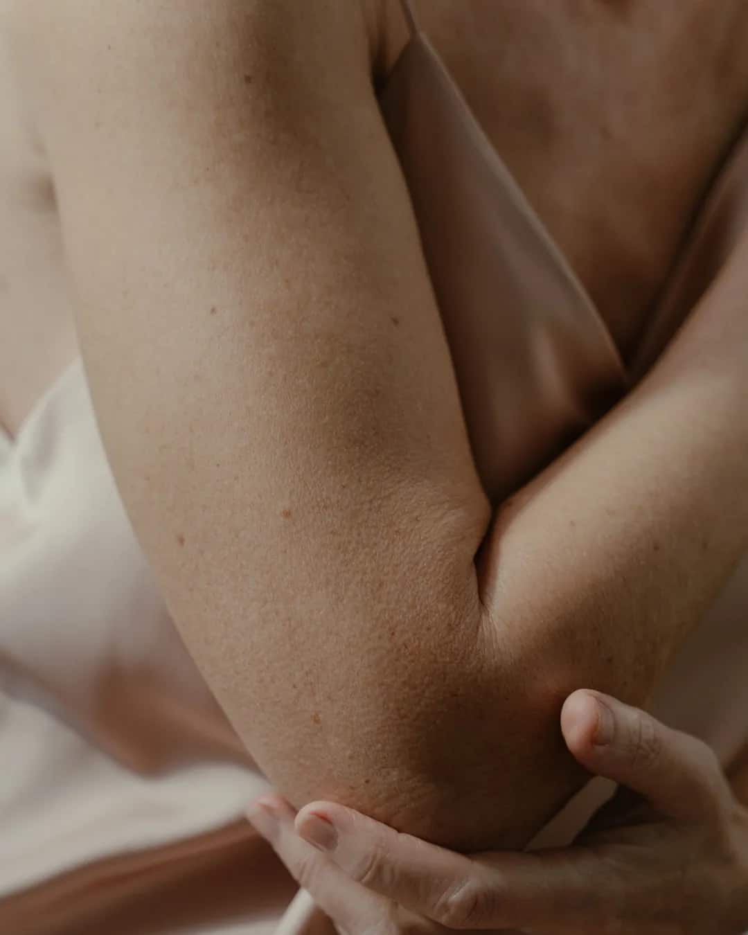 Upper arm and elbow of a woman in a silk camisole