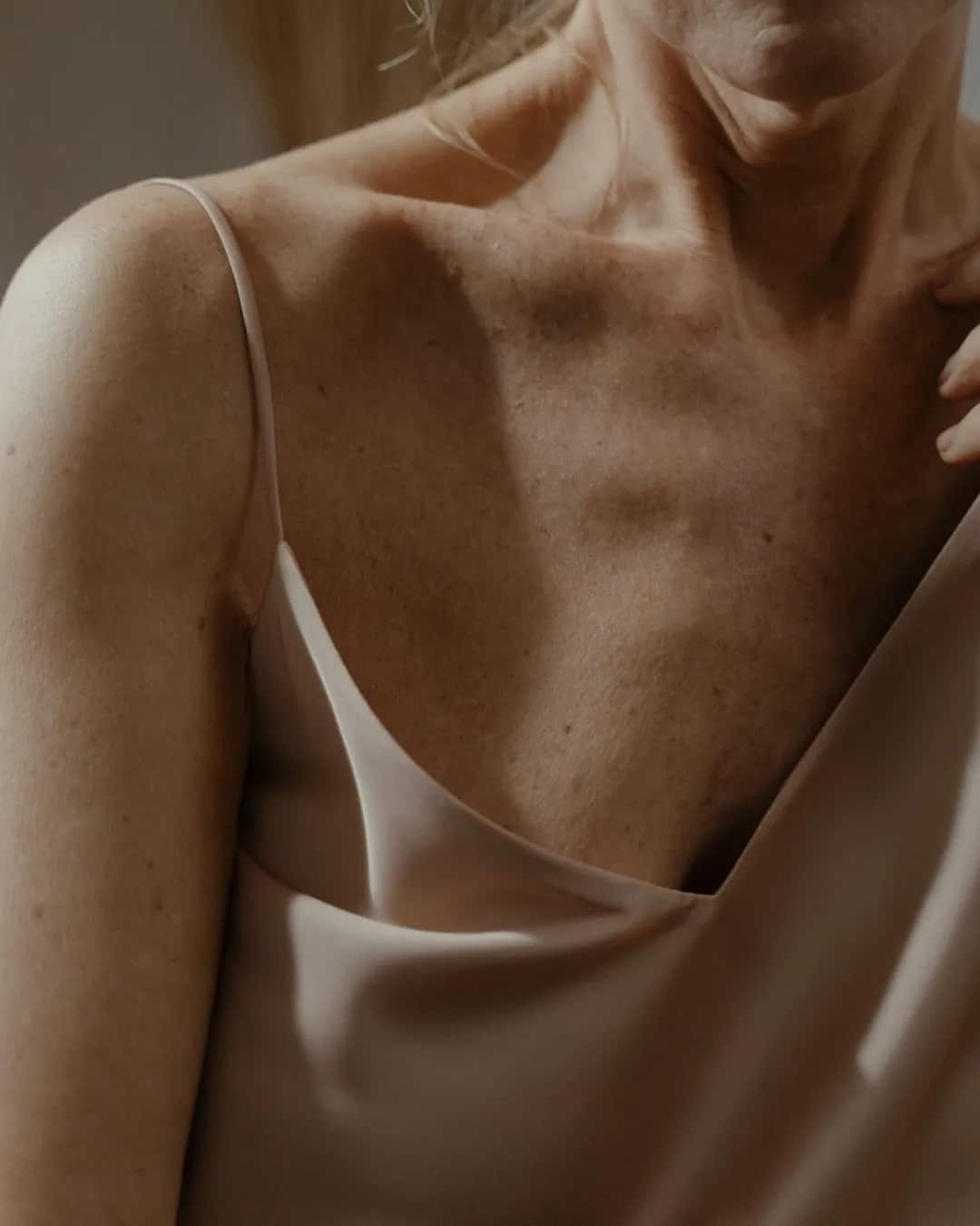 Chest and collarbones of a woman in a silk camisole, face out of frame